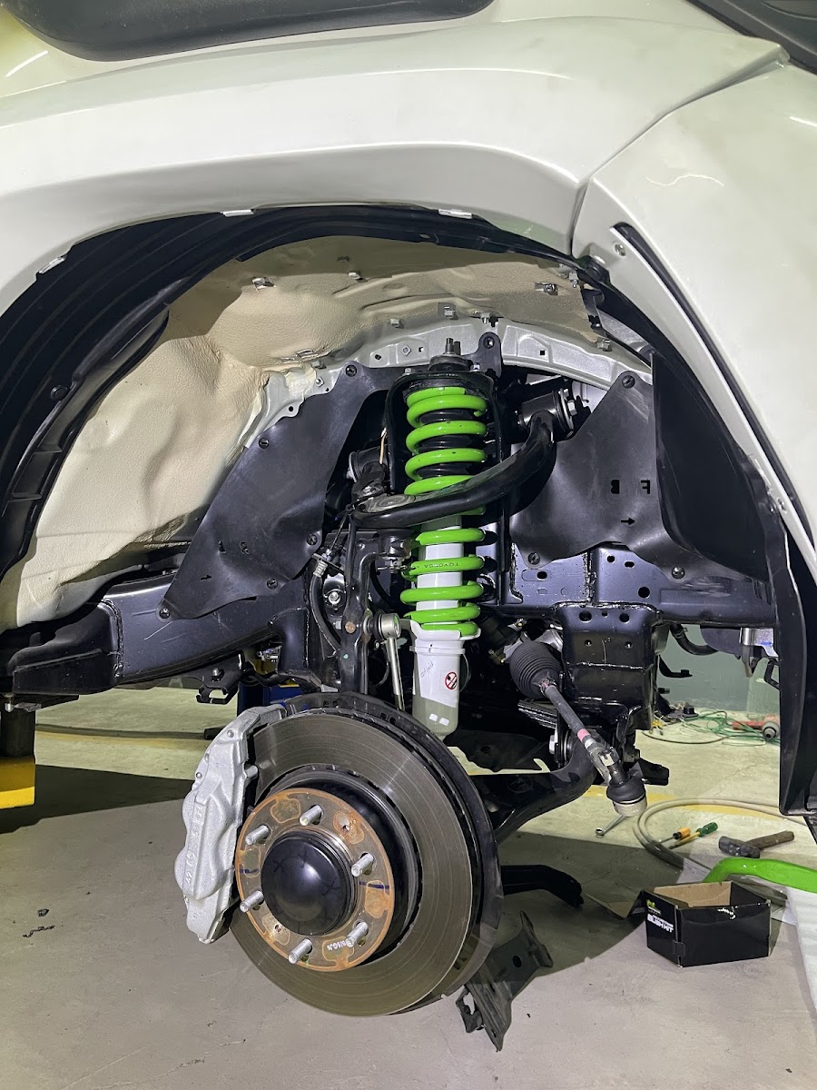 A TEIN coilover with green spring being fitted to a brake and suspension assembly at Drift Automotive